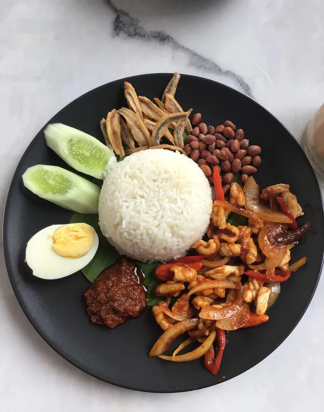 Overhead photo of a plate of nasi lemak with rice, egg, anchovies, peanuts, cucumber, sambal and squid